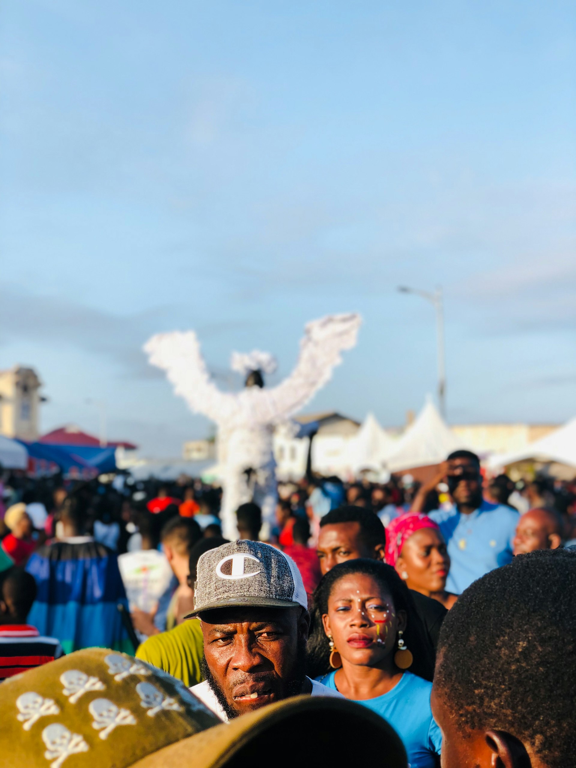 Golden-hour festival crowd with a winged stilt performer at Chale Wote in Jamestown, Accra